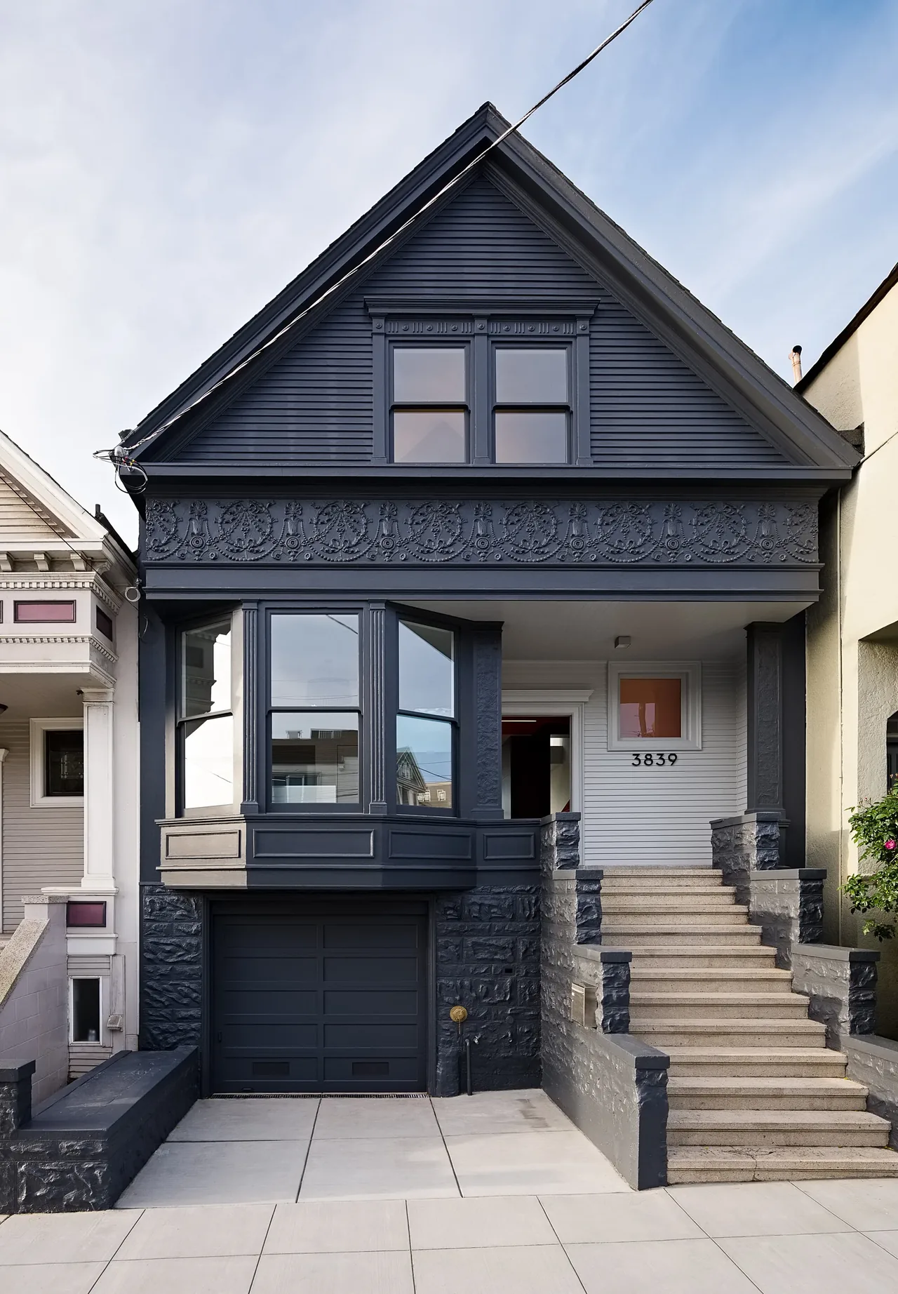 The CUT OUT HOUSE in San Francisco features dark siding with ornamental detailing and a prominent bay window over a garage.