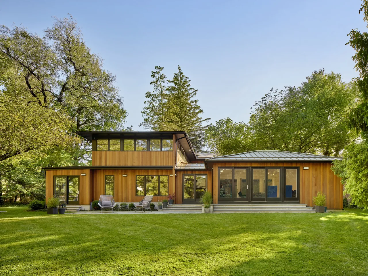 Rear exterior view of a modern wood house featuring floor-to-ceiling glazing and sliding glass doors.