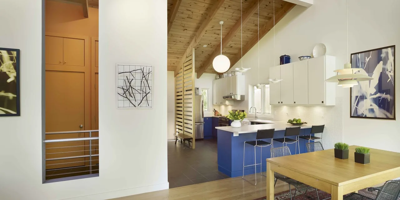 Kitchen and dining area under a vaulted wooden ceiling with exposed beams and modern furnishings.