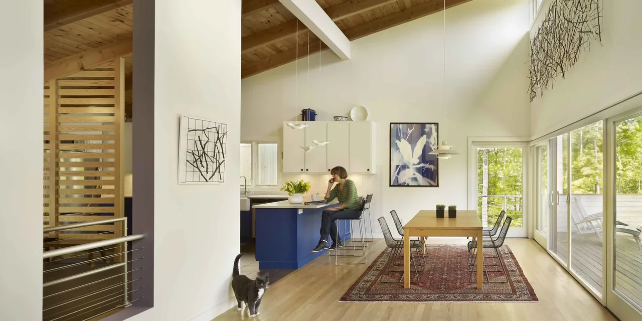 Interior dining and kitchen area with vaulted wood ceiling, exposed beams, clerestory windows, and floor-to-ceiling sliding glass doors to a deck.