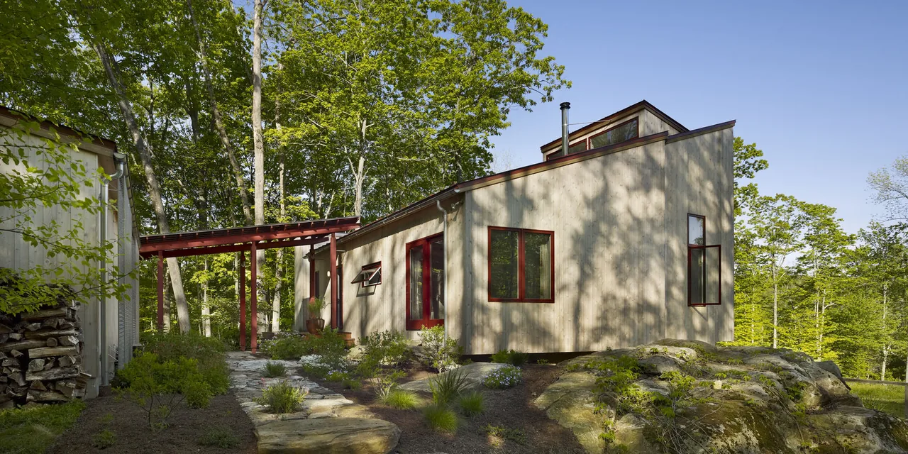 Modern house with vertical wood siding, clerestory windows, and a flat roof, set on a rocky landscape with surrounding trees.