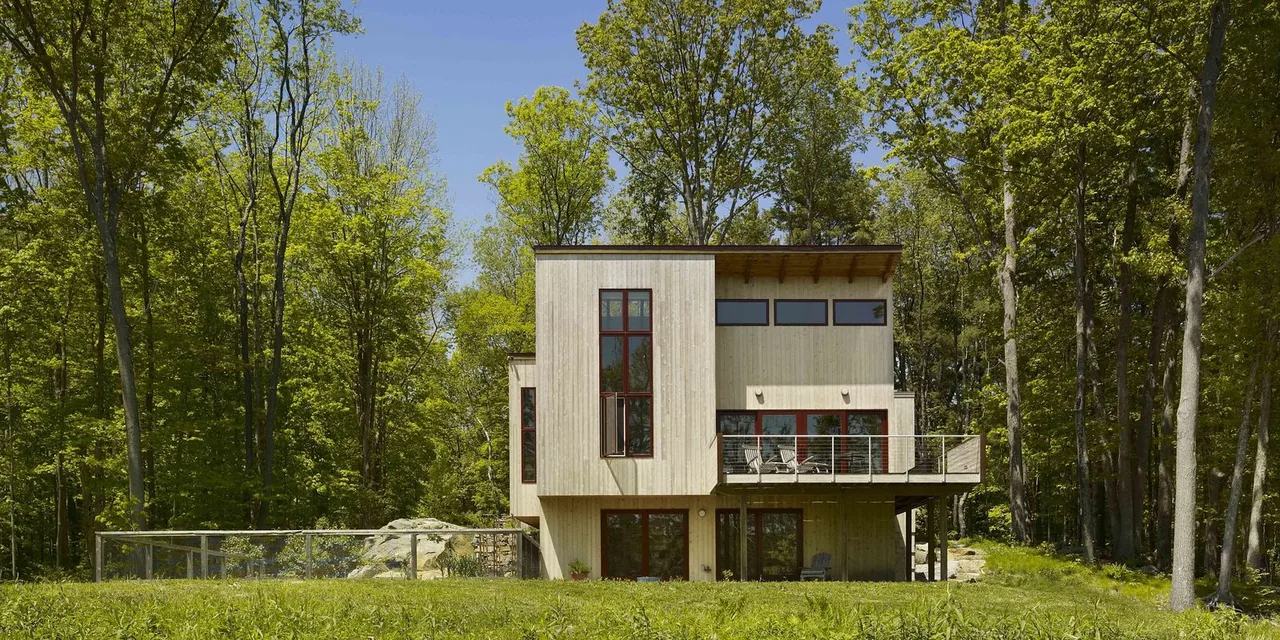 Rear exterior of a modern two-story house clad in vertical wood siding with floor-to-ceiling and clerestory windows and a balcony.