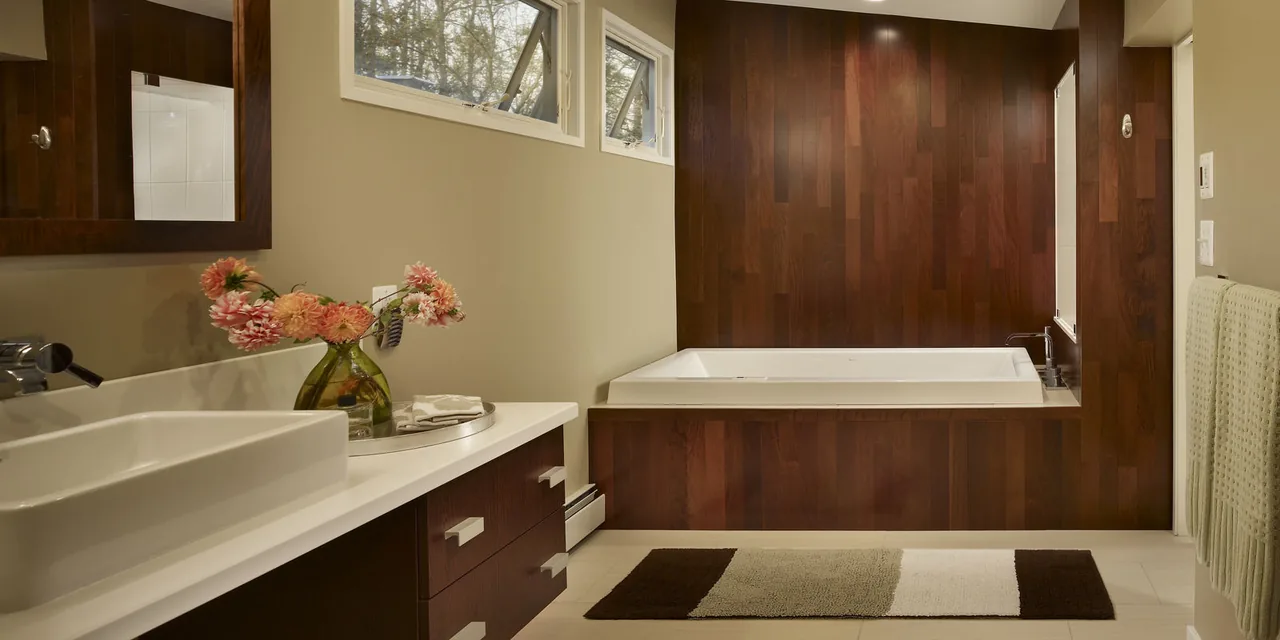 Bathroom interior with built-in bathtub surrounded by wood paneling and a rectangular sink on a wooden vanity.