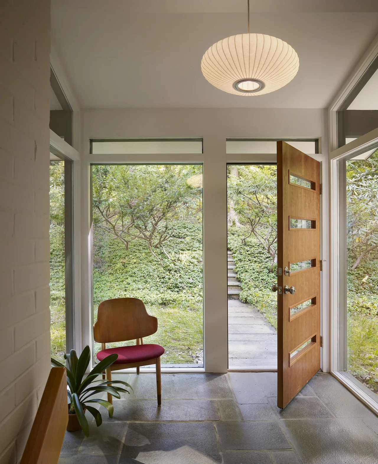 Entry room with open wooden door featuring horizontal glass panels and large windows overlooking greenery.