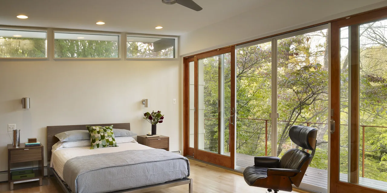 Bedroom with large wood-framed sliding glass doors, clerestory windows, and wood flooring.