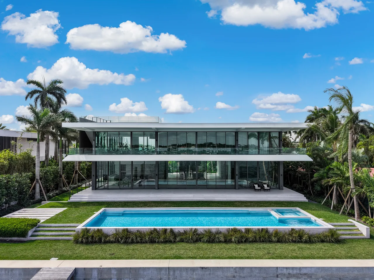 121 N Hibiscus Road features a modern design with floor-to-ceiling glass walls and a pool surrounded by tropical plants.