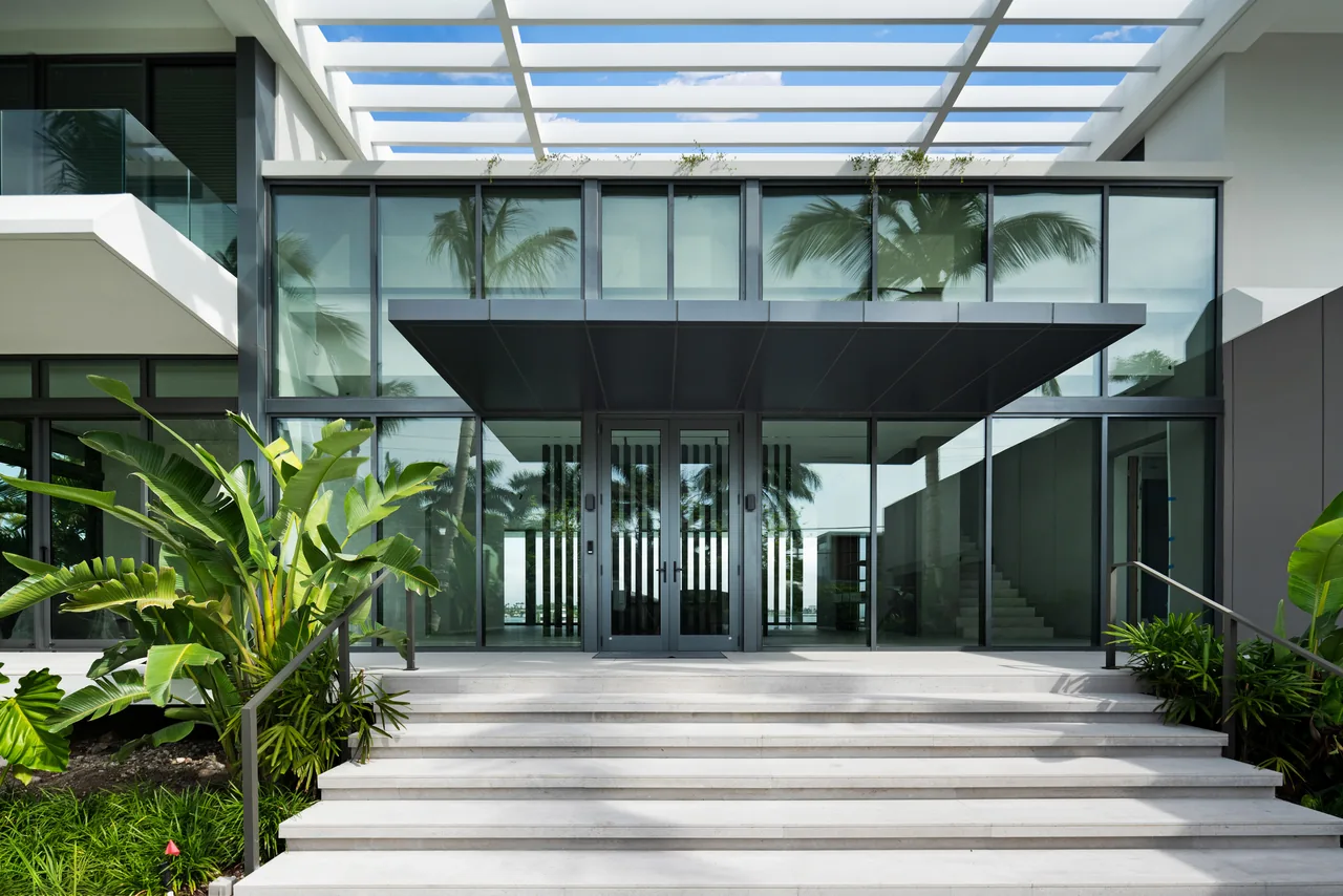 Exterior front entrance of 121 N Hibiscus Road by Touzet Studio featuring floor-to-ceiling glazing and a flat roof.