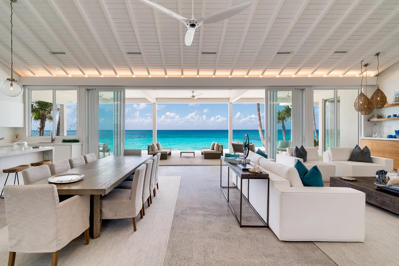 Open living and dining area with white ceiling beams and wide sliding glass doors overlooking the ocean at Cat Cay Residence.
