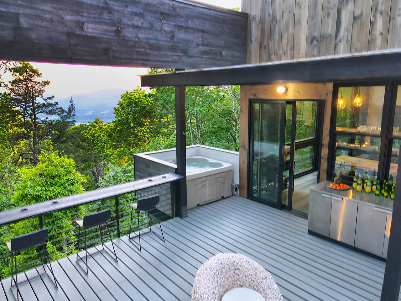Deck features a hot tub, seating with bar stools along a railing counter, and access through sliding glass doors to the interior.