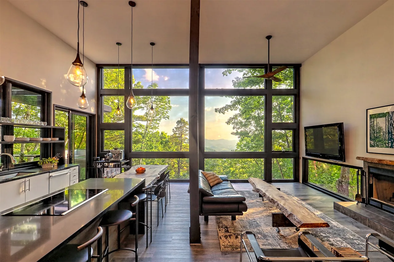 Open living room and kitchen with floor-to-ceiling glazing and views of a forested hill landscape.