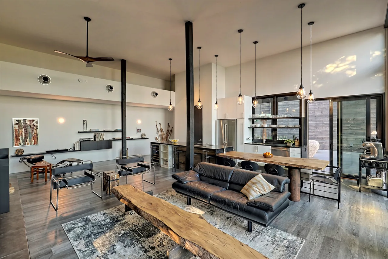 Modern open living and kitchen space with live edge wood furniture, black metal accents, and pendant lighting.