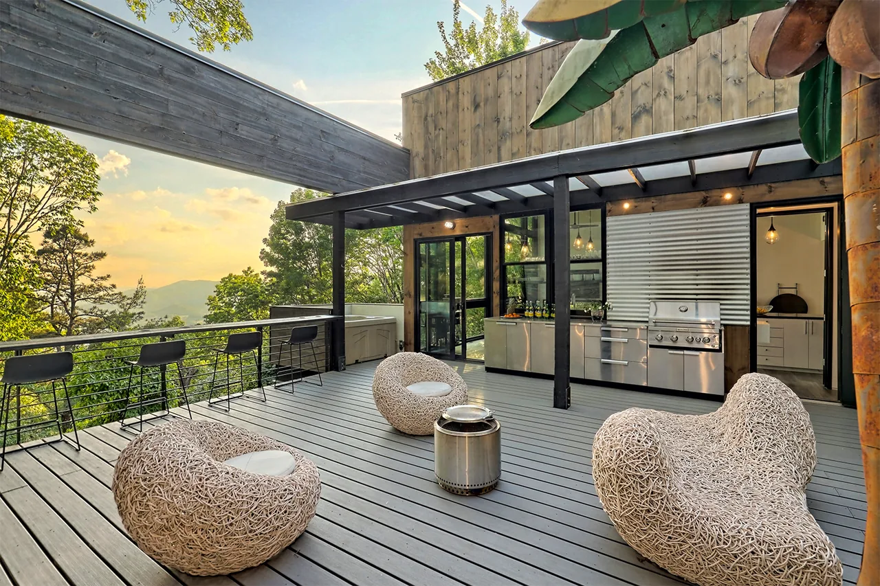 Outdoor living patio featuring woven lounge chairs and a stainless steel grill with a scenic tree view at sunset.