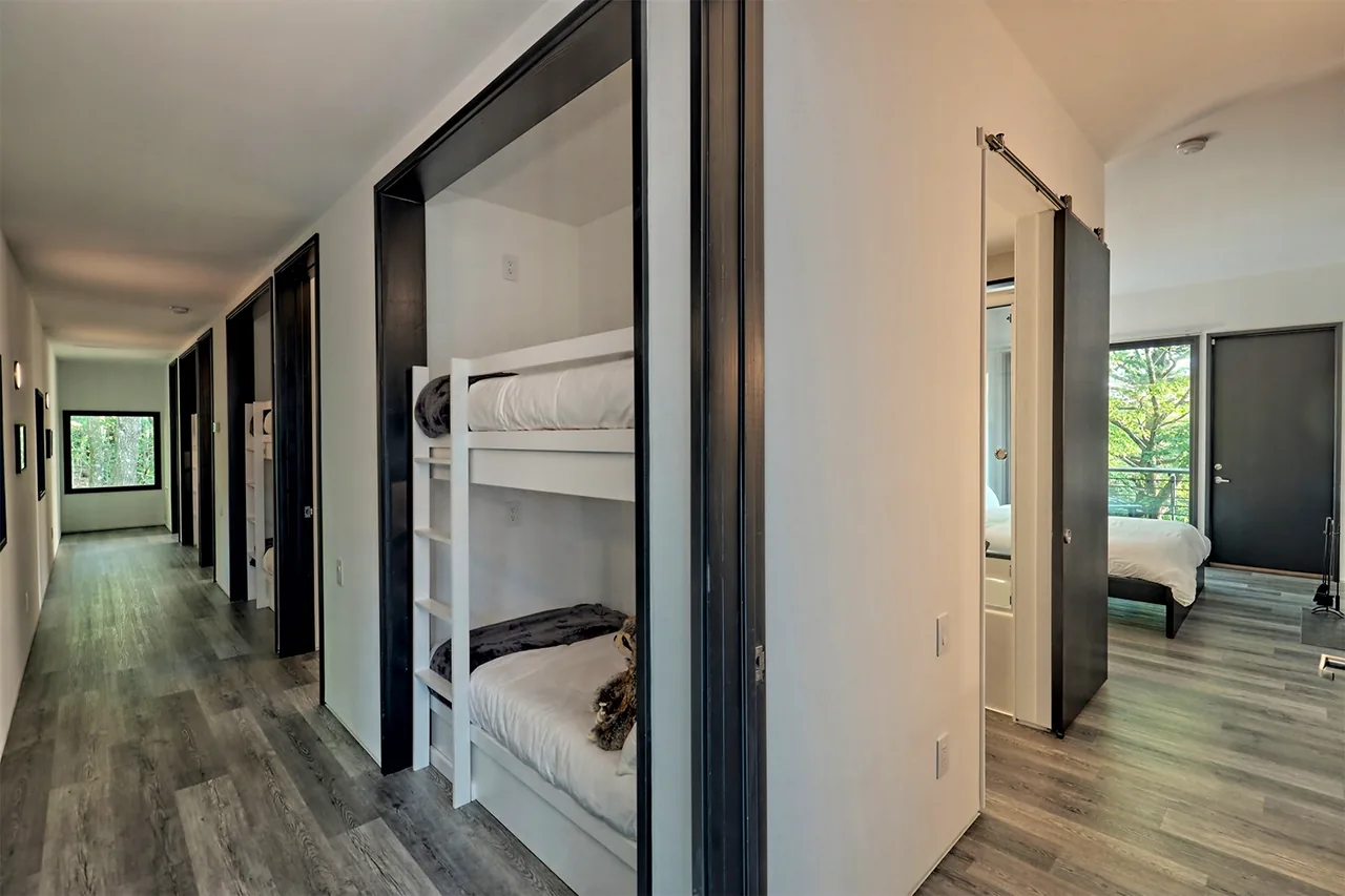 Interior view of hallway with bunk beds in a nook and a bedroom at the end with large window and door