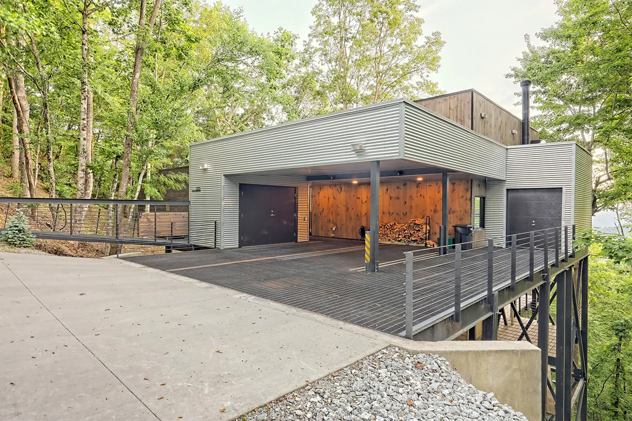 Elevated modern house with corrugated metal siding, an open carport area, and metal deck railing.