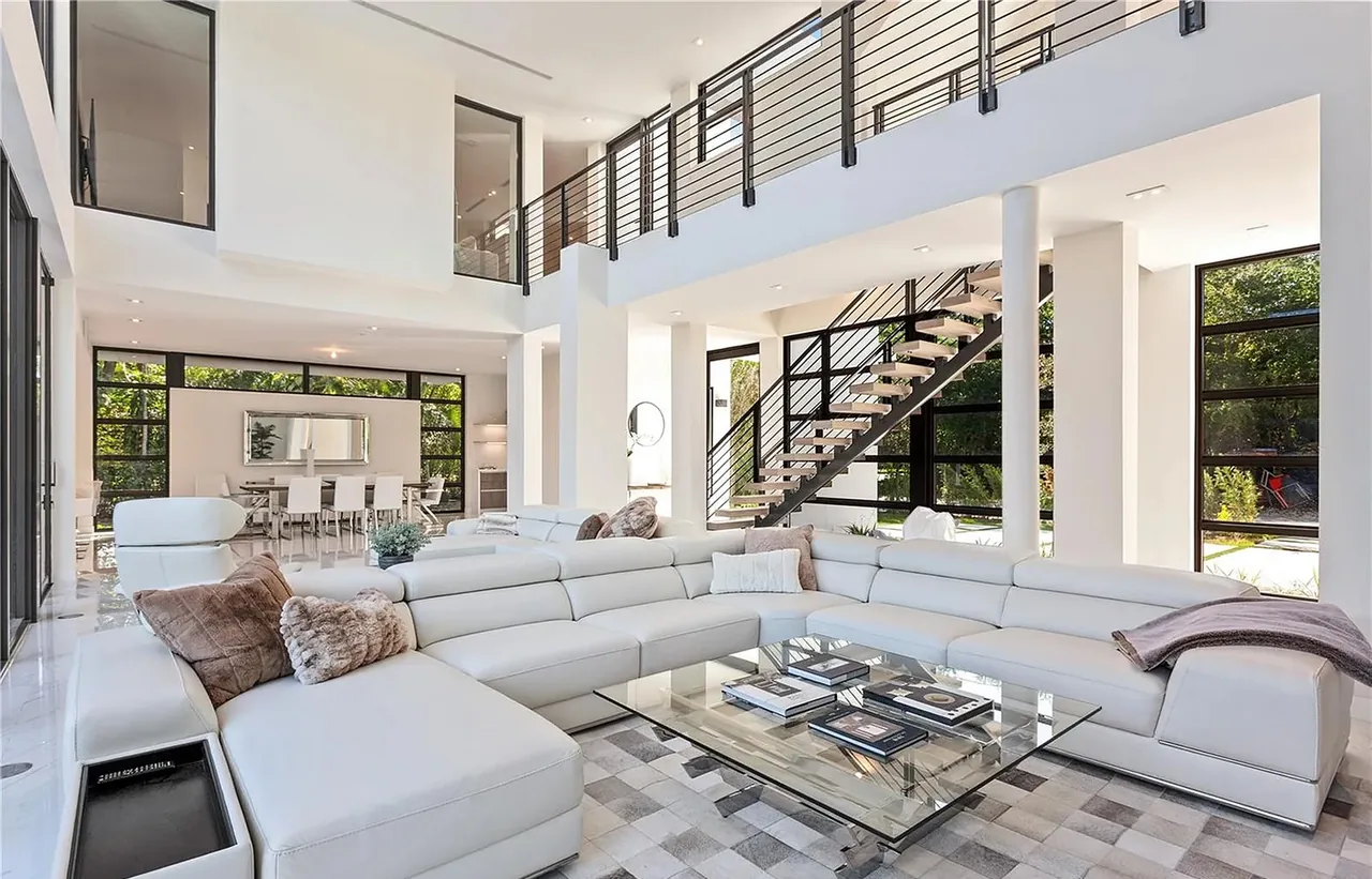 Living room features a white leather sectional sofa and black metal railing staircase with wood treads overlooking a dining area.