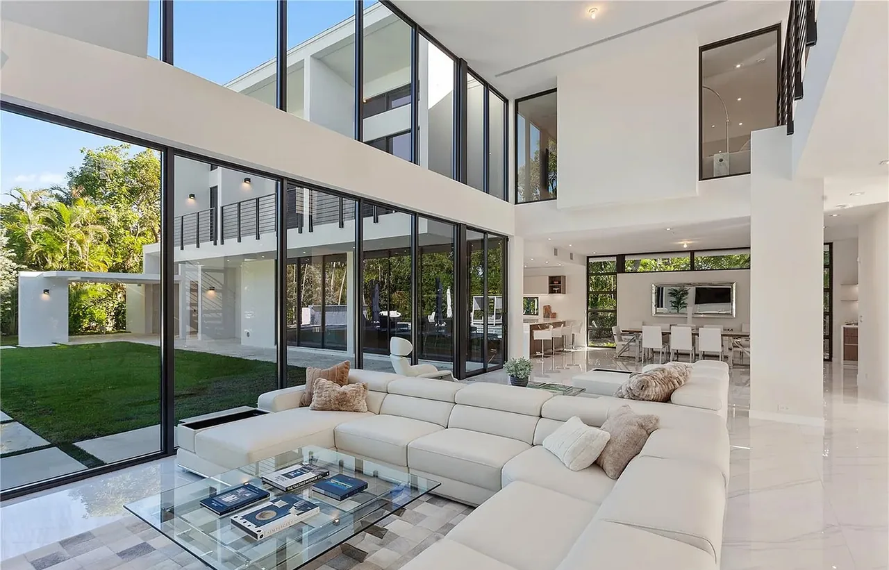 CASA MARIOLA's living room features expansive floor-to-ceiling glass glazing and a floating staircase visible near the upper level.