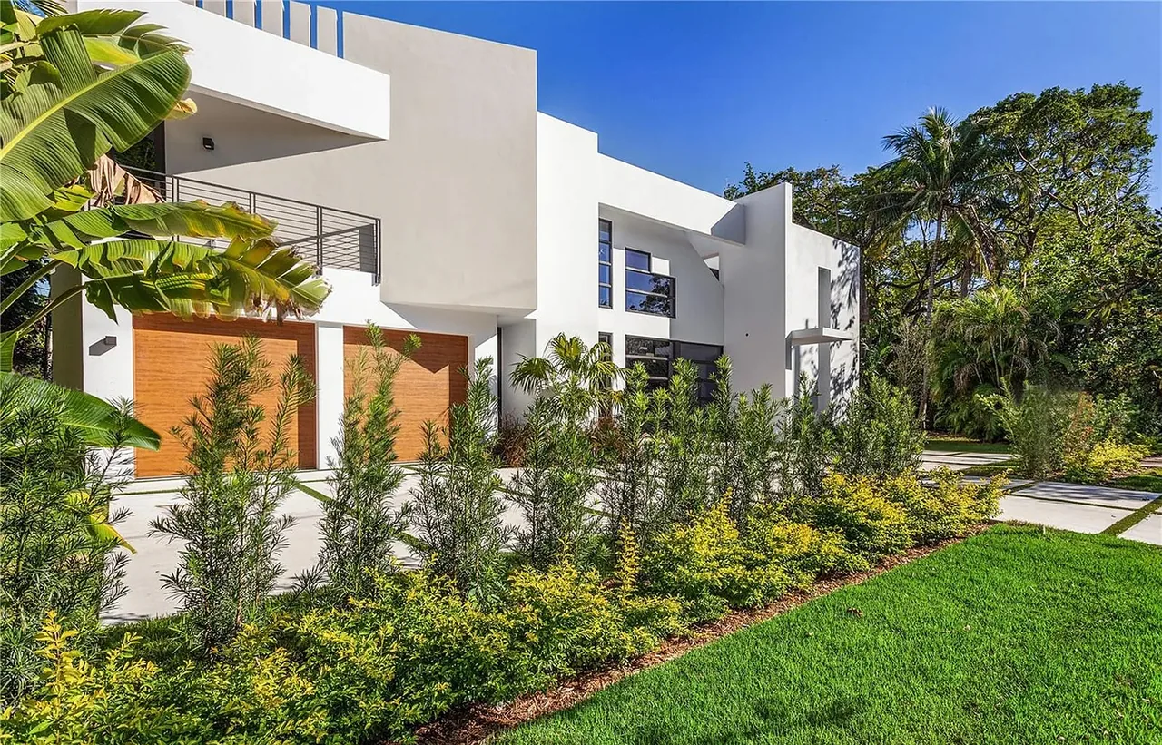 CASA MARIOLA features a modern exterior with flat roof and wood garage doors set amidst dense landscaping.