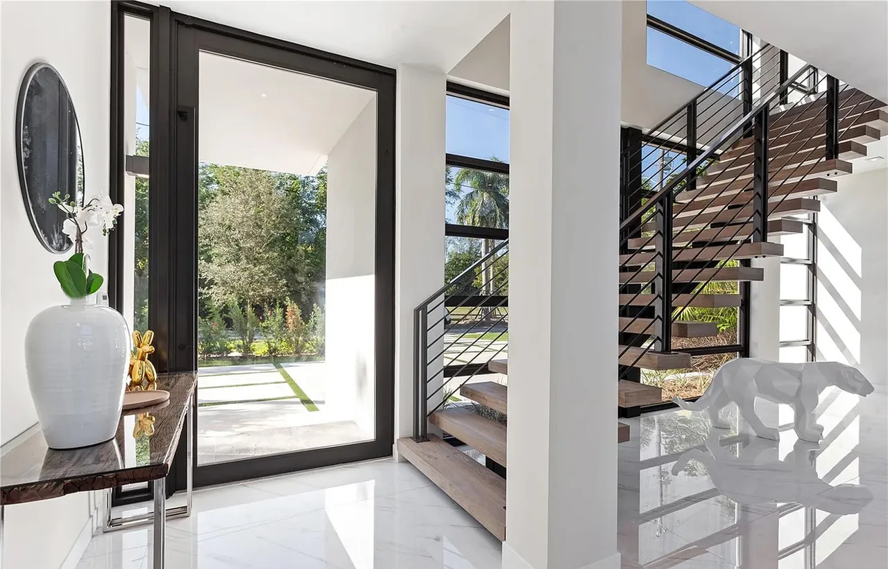 Entry area features floating wood stairs with black metal railings and a large black-framed glass door revealing the outdoors.