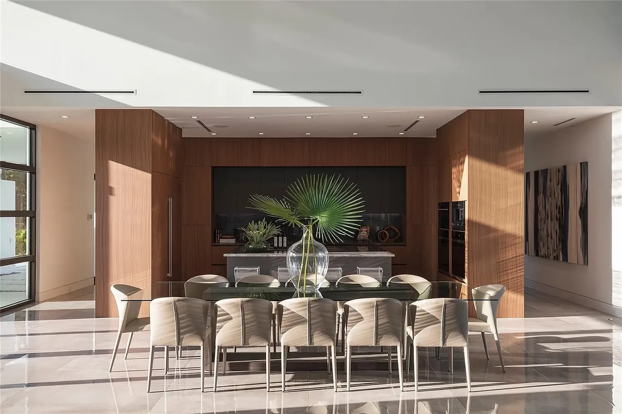 Dining space features a glass table with beige chairs adjacent to a wood-paneled kitchen in CASA BARSKY.