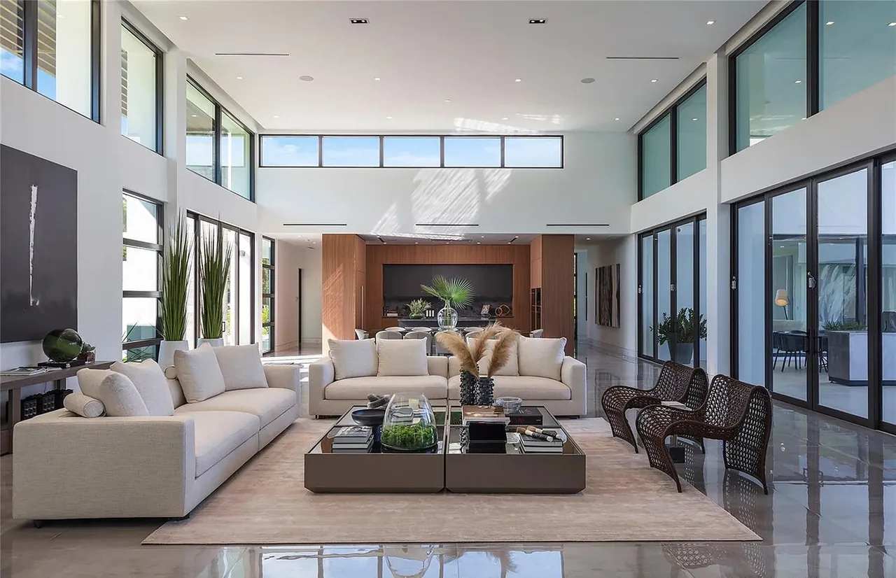 Modern living room in CASA BARSKY, featuring floor-to-ceiling windows and high ceilings with recessed lighting.