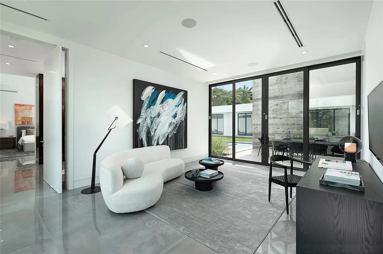 Living room with polished gray floor tiles, white curved sofa, abstract wall art, and floor lamp, opening to an outdoor seating area through sliding glass doors.