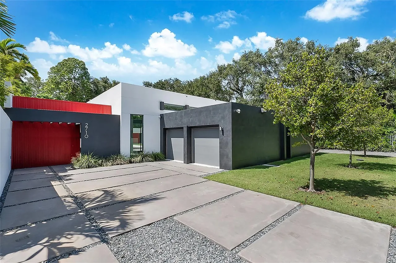 Modern flat-roofed house with black and white exterior walls and a red gate under a blue sky.