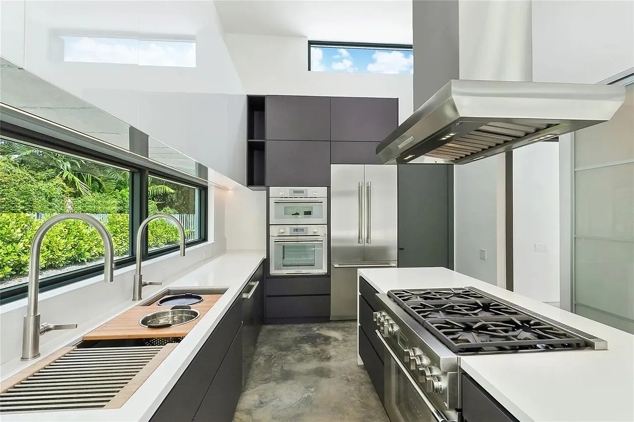 The kitchen in CASA BOUGAINVILLEA features black cabinetry, a built-in oven, and a gas range with a stainless steel hood under clerestory windows.