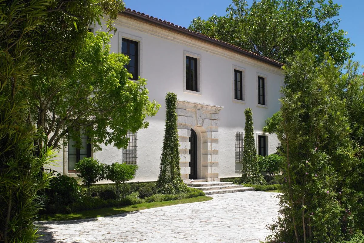 Exterior front view of the Flamingo Road Residence showing arched stone doorway and stucco walls with black window frames.