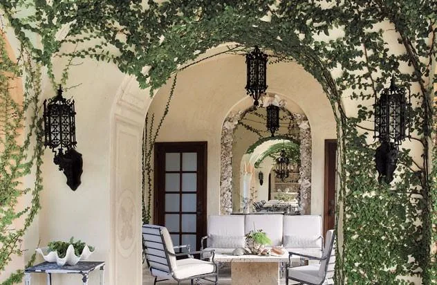 Covered patio at Flamingo Road Residence features arched openings, stone steps, and black decorative lanterns with wall sconces.