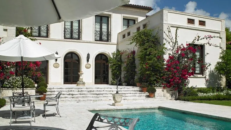 The Flamingo Road Residence features a pool and stone steps leading to a stucco exterior with arched windows and climbing vines.