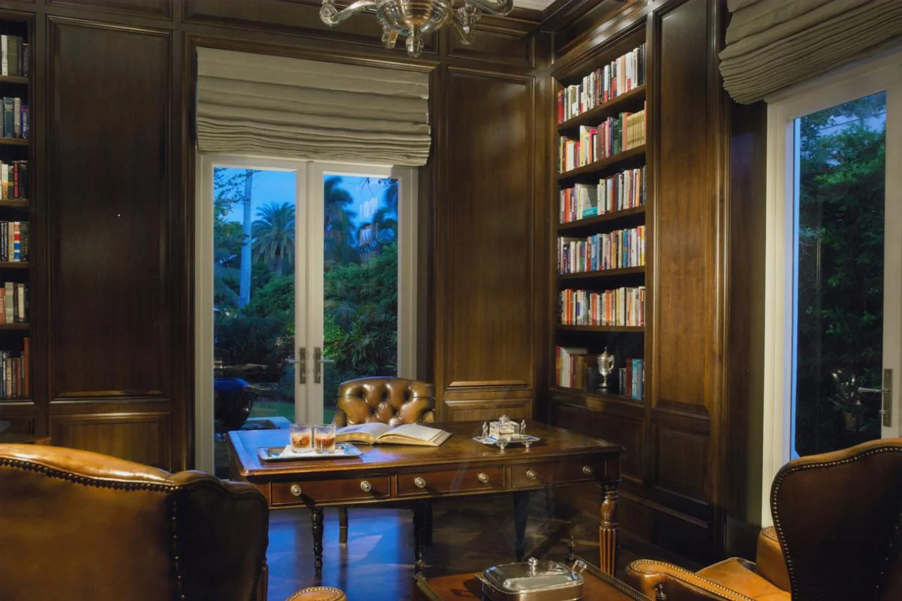 The Sunset Island Residence study features rich wood paneling, built-in bookshelves, and leather seating facing French doors.