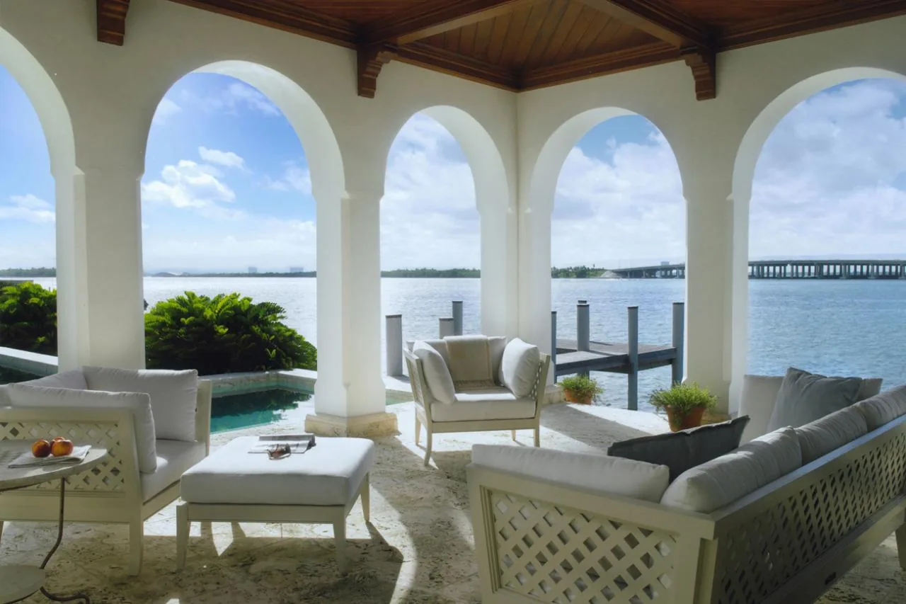 The Sunset Island Residence features an arched hallway on its outdoor covered patio with views of the water and a dock.