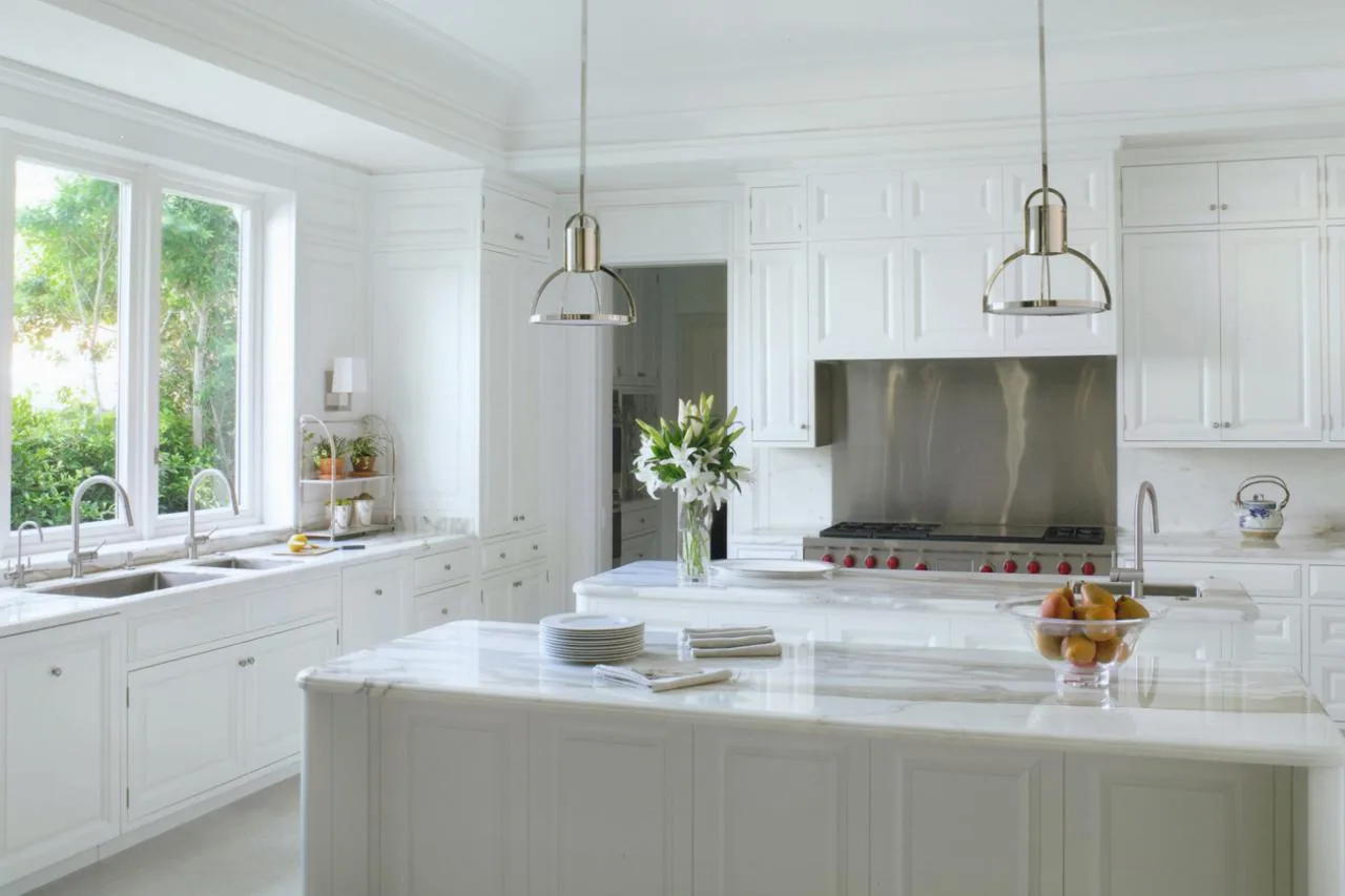 This kitchen in the Sunset Island Residence features white cabinetry, marble countertops, and stainless steel appliances with pendant lighting.