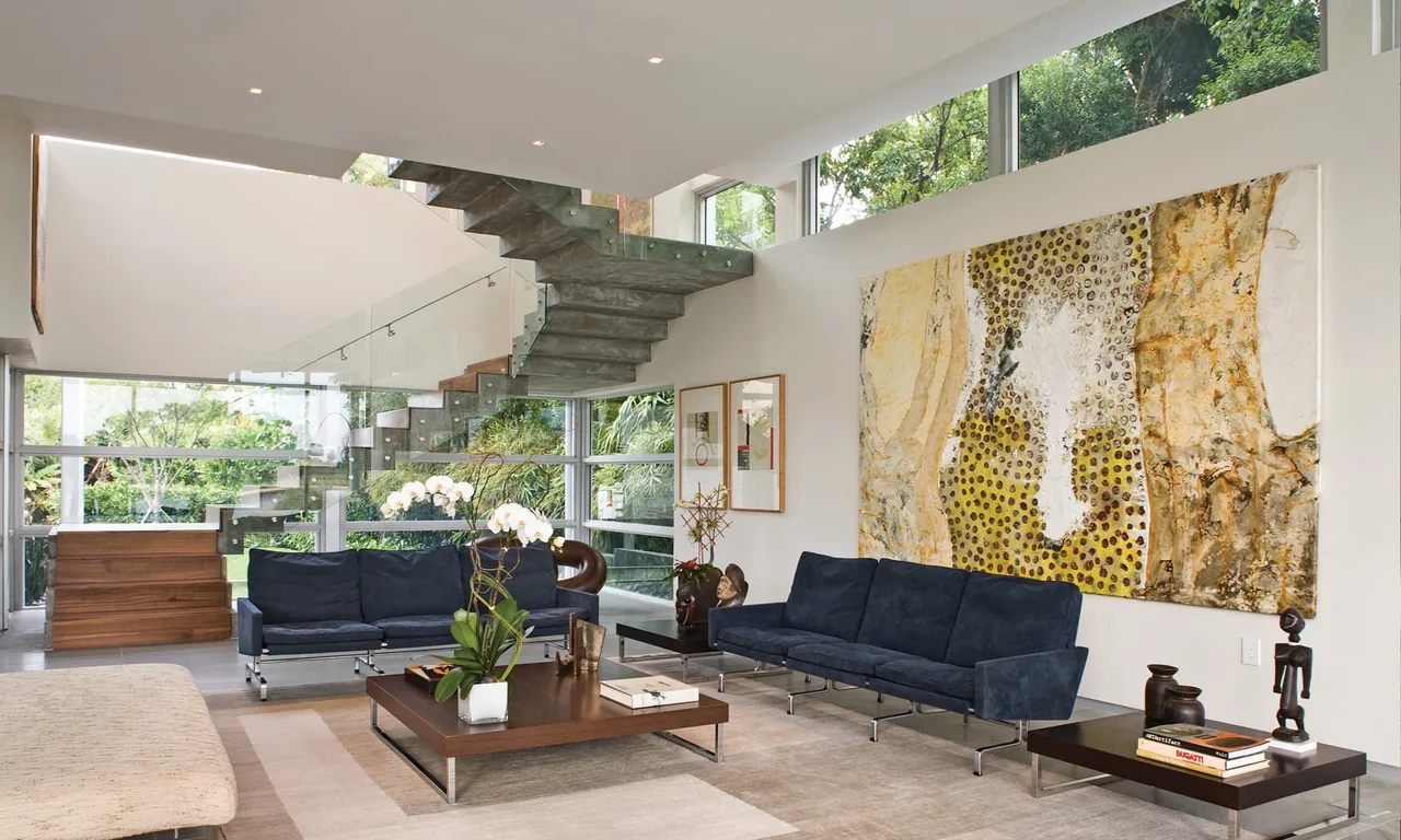Living room featuring floating concrete staircase with glass railing and floor-to-ceiling windows.