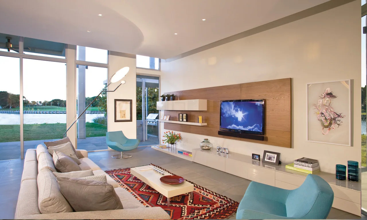 Living room with large glass windows providing a water view, built-in media cabinetry, and contemporary furniture.