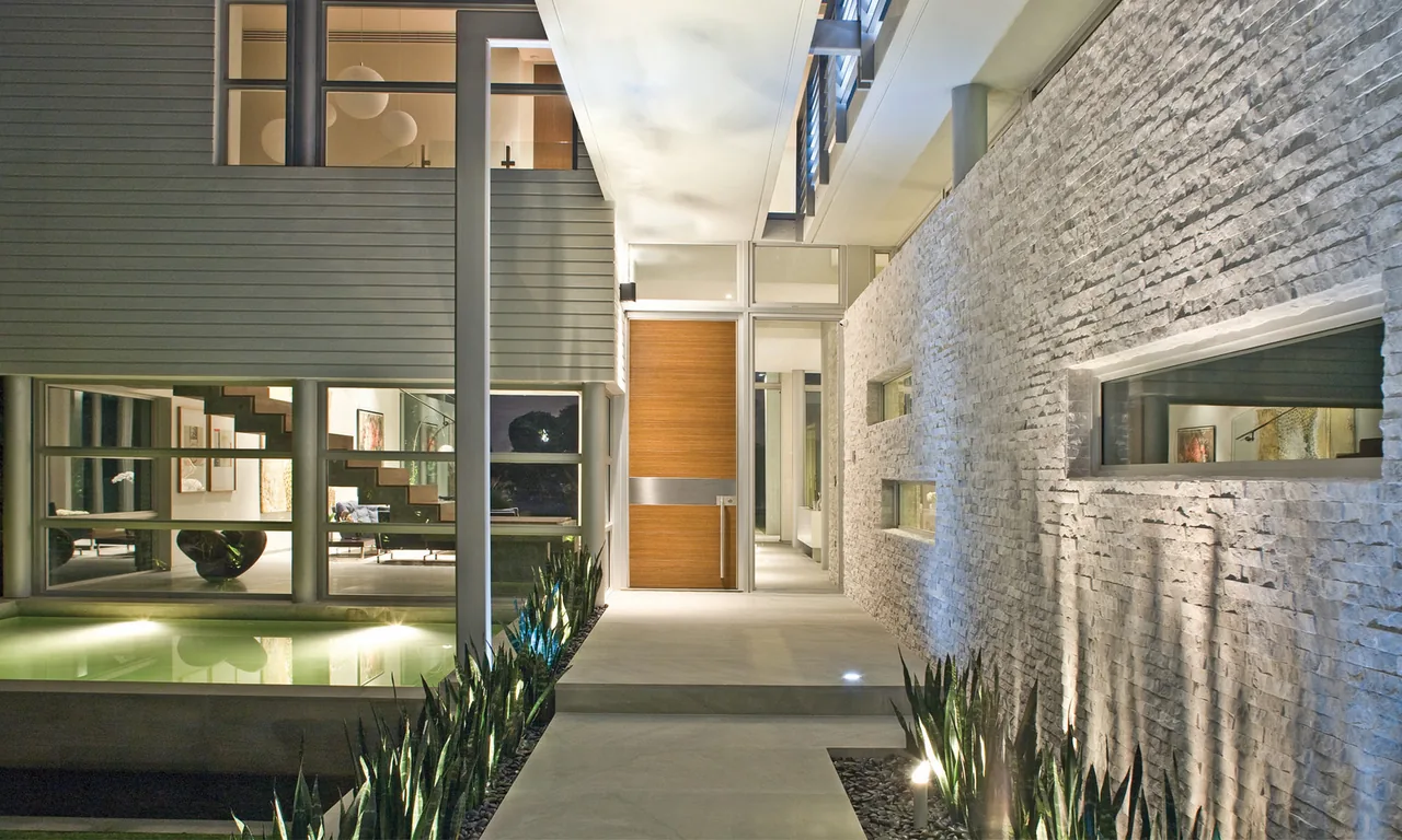 Modern architecture courtyard entrance featuring vertical columns, horizontal strip windows, stone wall cladding, and landscape lighting at night.