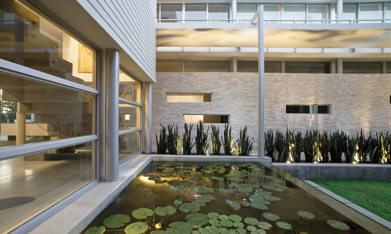 Courtyard exterior view with rectangular water pond, plants, and modern architectural elements.