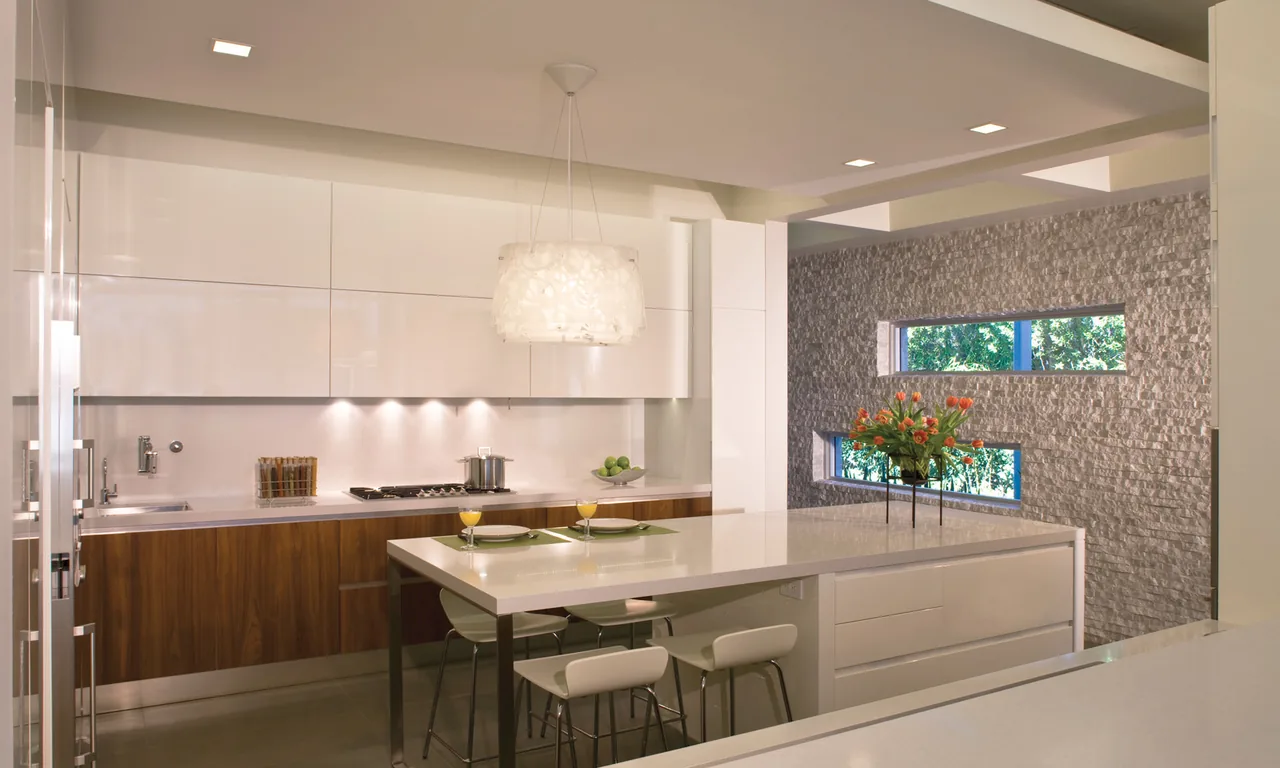 Modern kitchen featuring a large island, textured stone accent wall with horizontal windows, and white and wood cabinetry.
