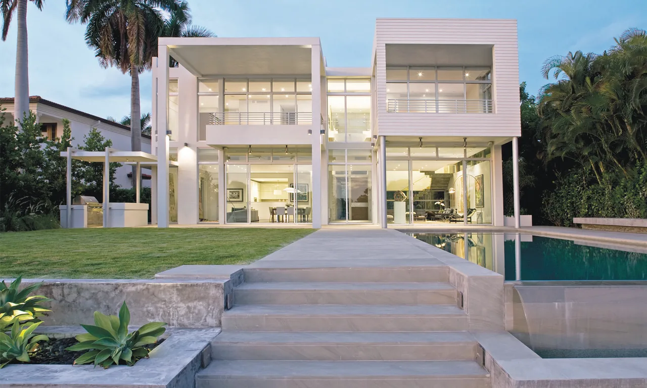 Exterior front view of a modern house featuring floor-to-ceiling glazing, vertical columns, and a reflecting pool.