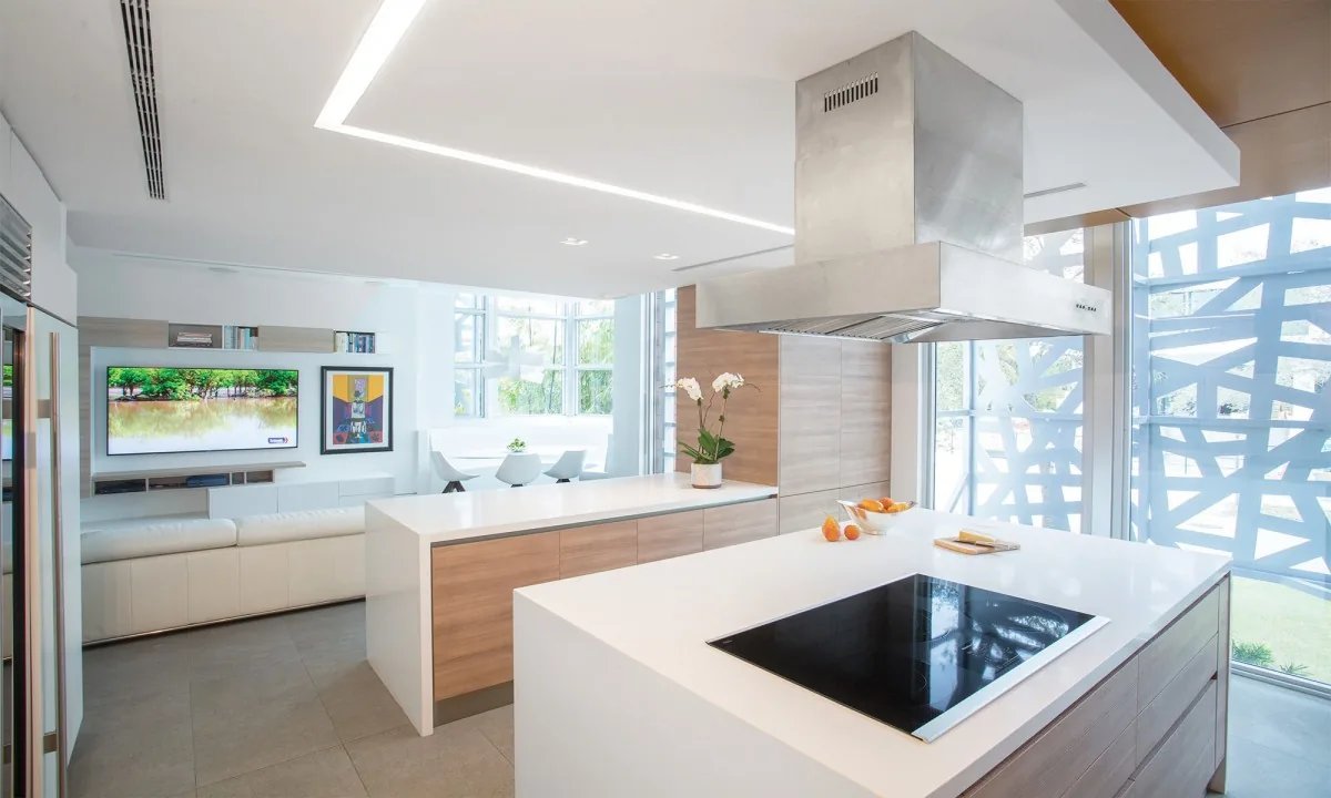 Bright kitchen with wood cabinets, white quartz countertops, and stainless steel range hood by a window with decorative screen.