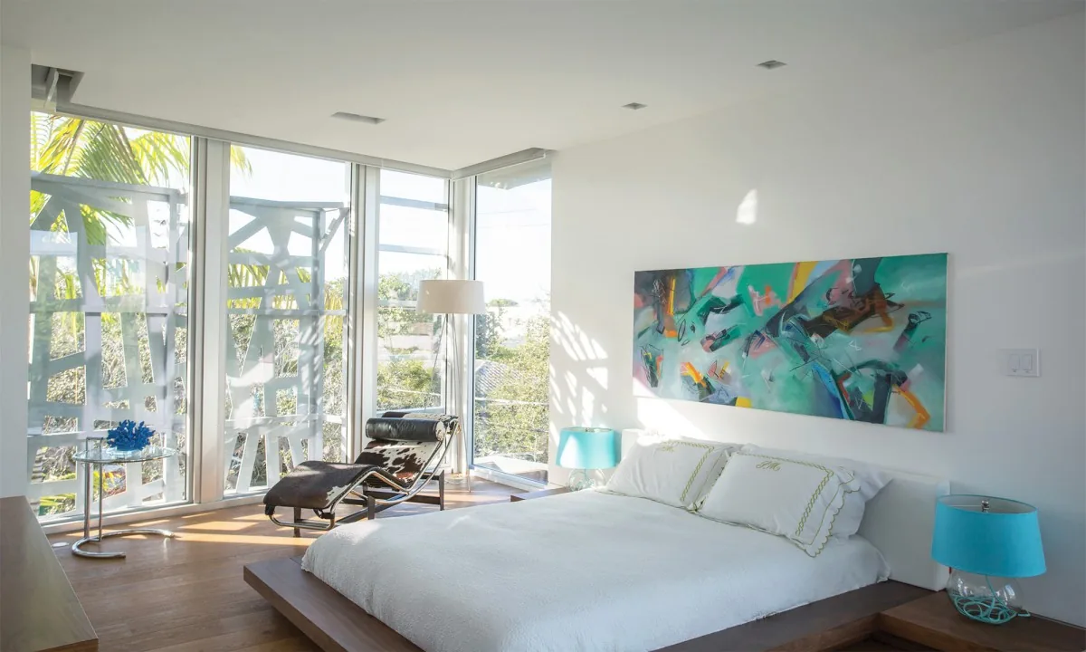 Woodcrest bedroom features floor-to-ceiling corner glazing, a wooden platform bed, and vibrant abstract artwork on the wall.