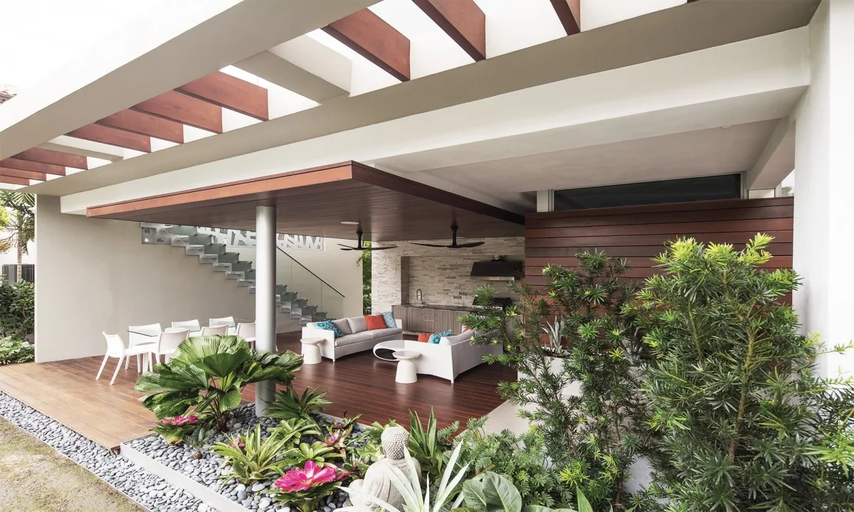 Outdoor living area features a wooden deck, glass-railing staircase, white seating, and an open pergola providing partial shade.