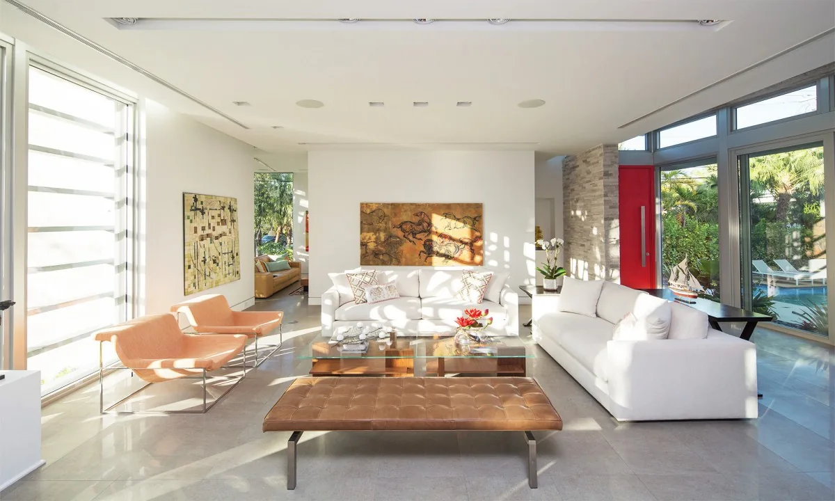 Living room featuring two white sofas, a glass coffee table, and large windows overlooking a pool area.