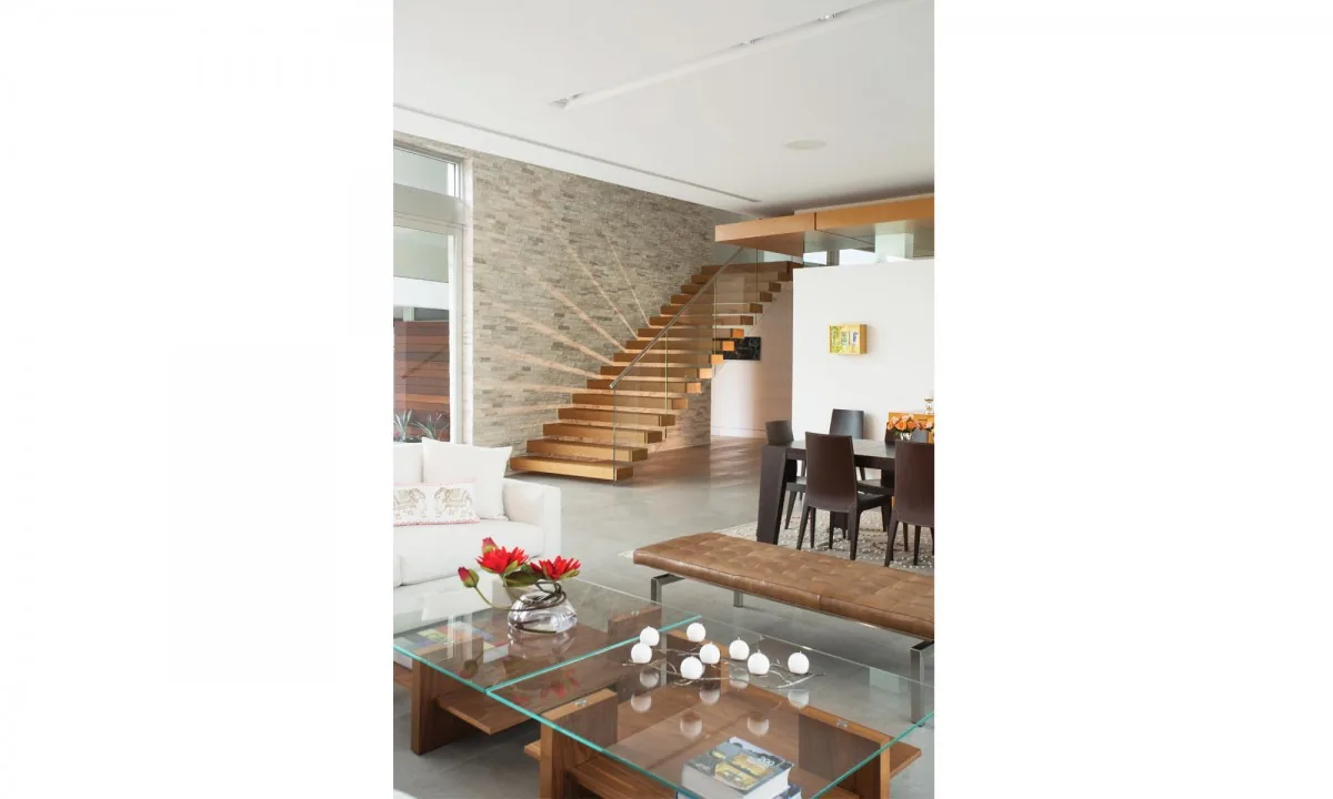 Living and dining area with floating staircase, glass railing, and minimalist furnishings in the WOODCREST project by KZ Architecture.