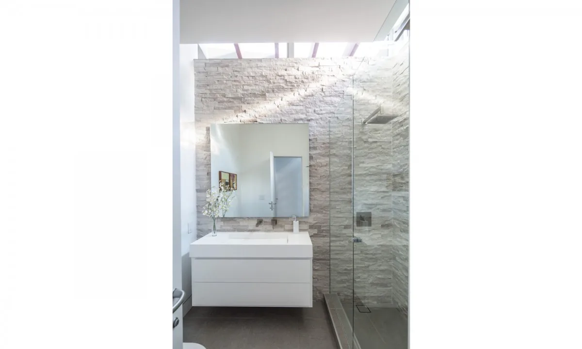 Bathroom with floating vanity, stone textured accent wall, and glass shower enclosure.