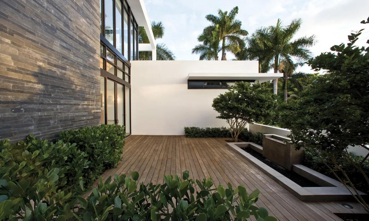 Covered patio area with wood deck flooring next to stone and glass exterior walls.
