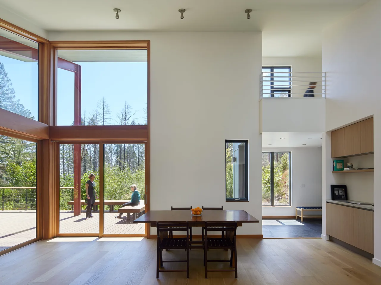 Dining area with floor-to-ceiling glazing opening to a deck and high ceilings.