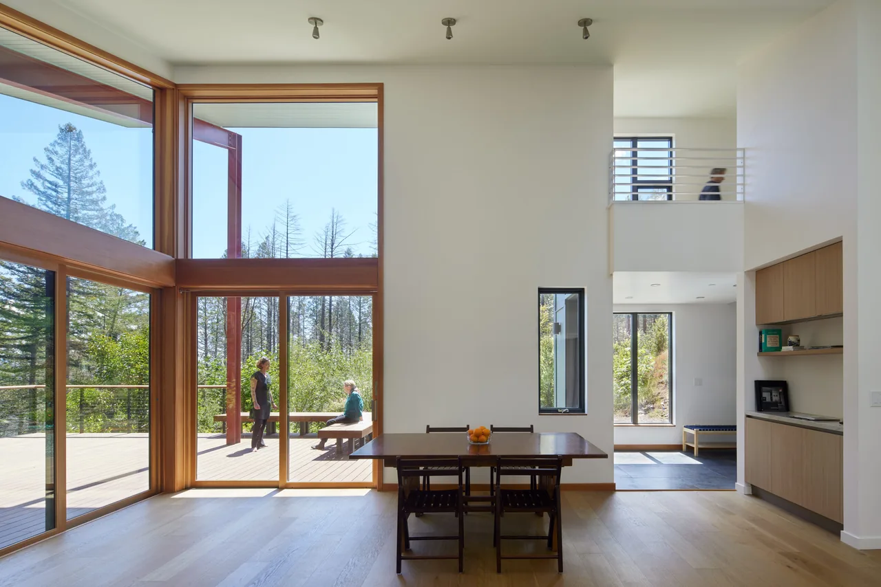 Dining area with wooden floors and large floor-to-ceiling glazing opening to an outdoor deck area.
