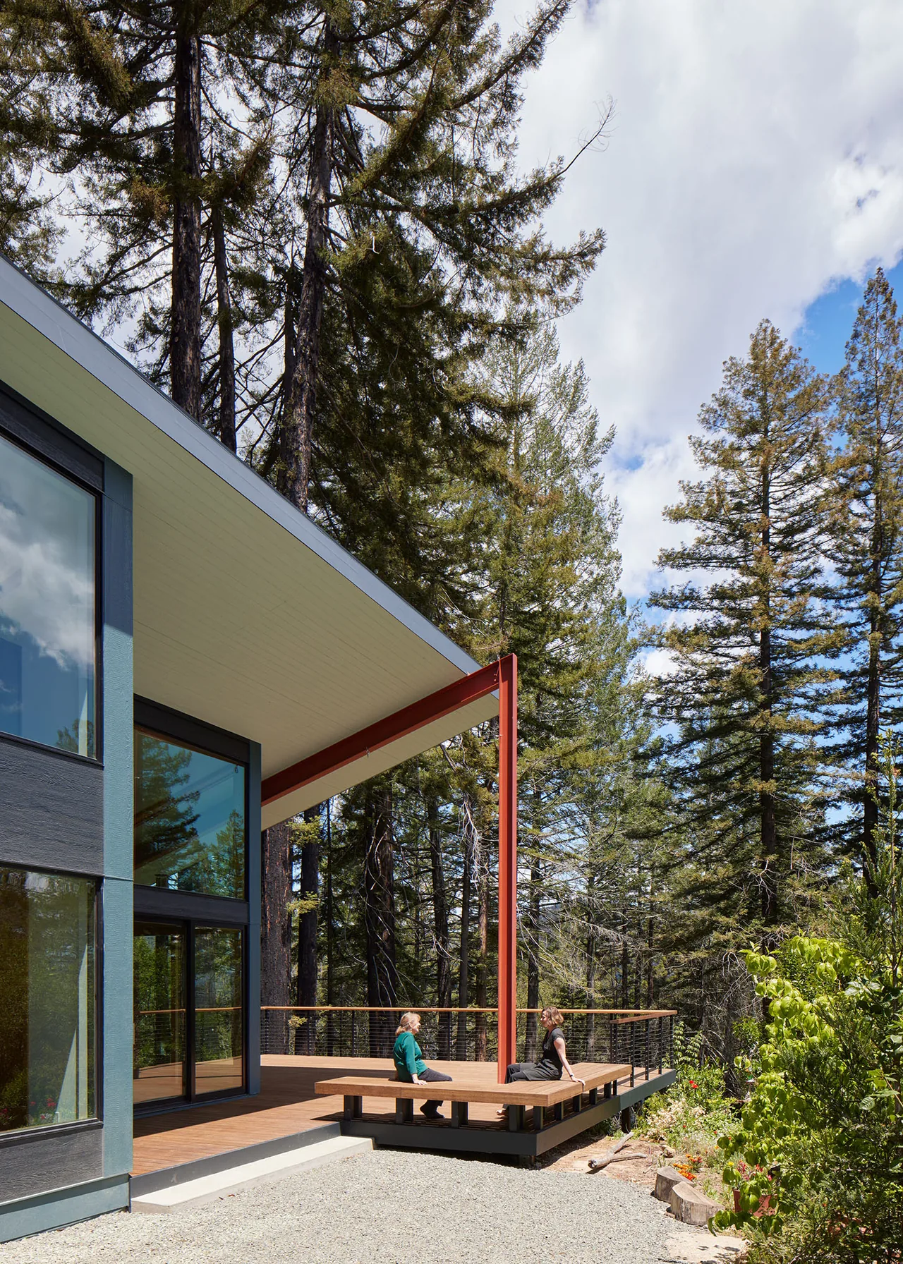 A modern house deck with built-in seating and cable railing overlooking a wooded landscape.