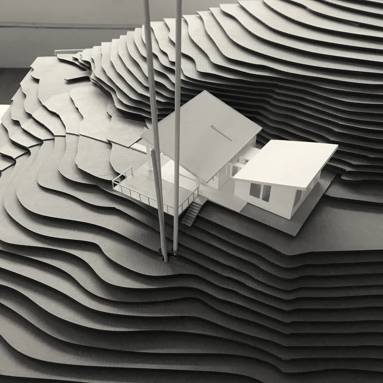 Architectural model showing a modern two-building house with a butterfly roof and flat roof on a contoured terrain model.